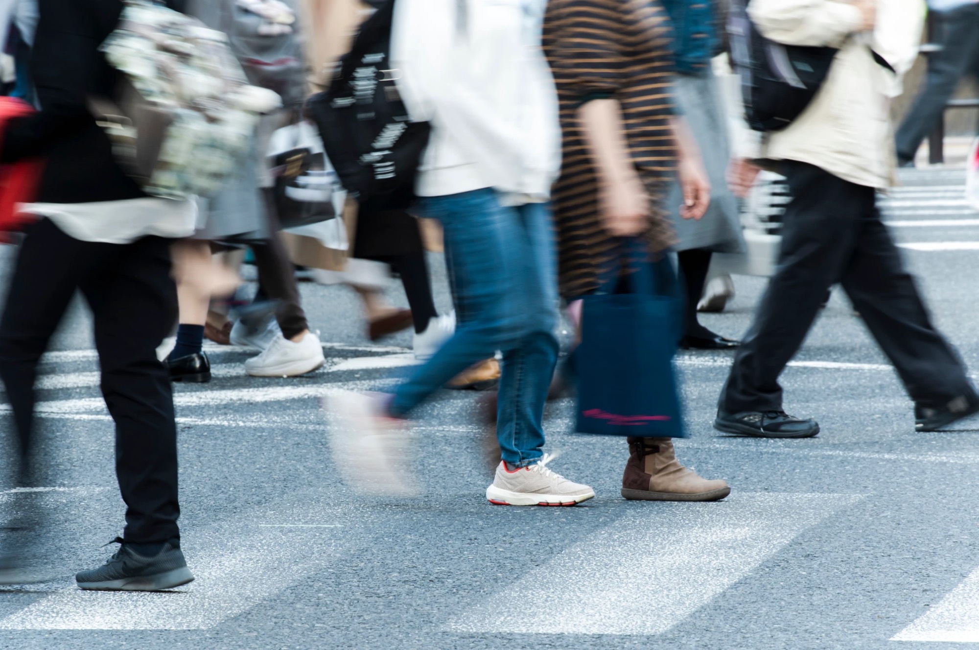 A crowd of people crossing a busy street, blurred in motion